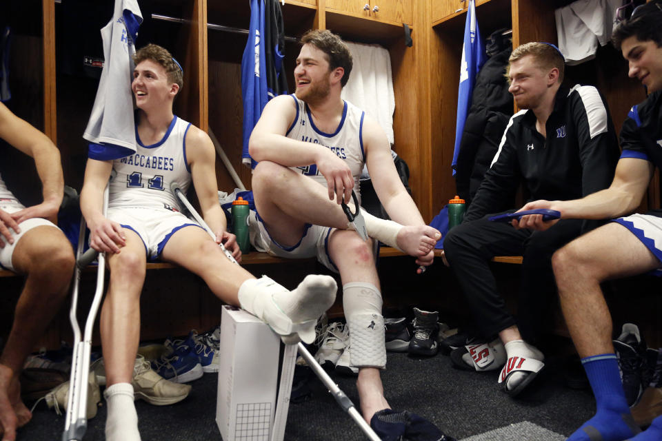 Guard Ryan Turell and forward Daniel Katz, who were injured in a game against Farmingdale, joke with teammates in the locker room at Yeshiva University in New York, Feb. 22, 2020. (AP Photo/Jessie Wardarski)