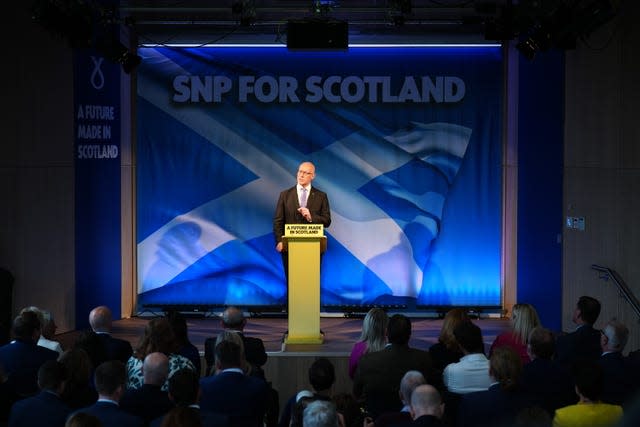 John Swinney addresses an SNP audience from a stage with the Saltire flag as the backdrop