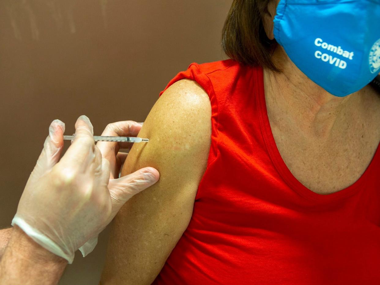 woman getting her COVID shot with face mask on that says 'combat COVID'