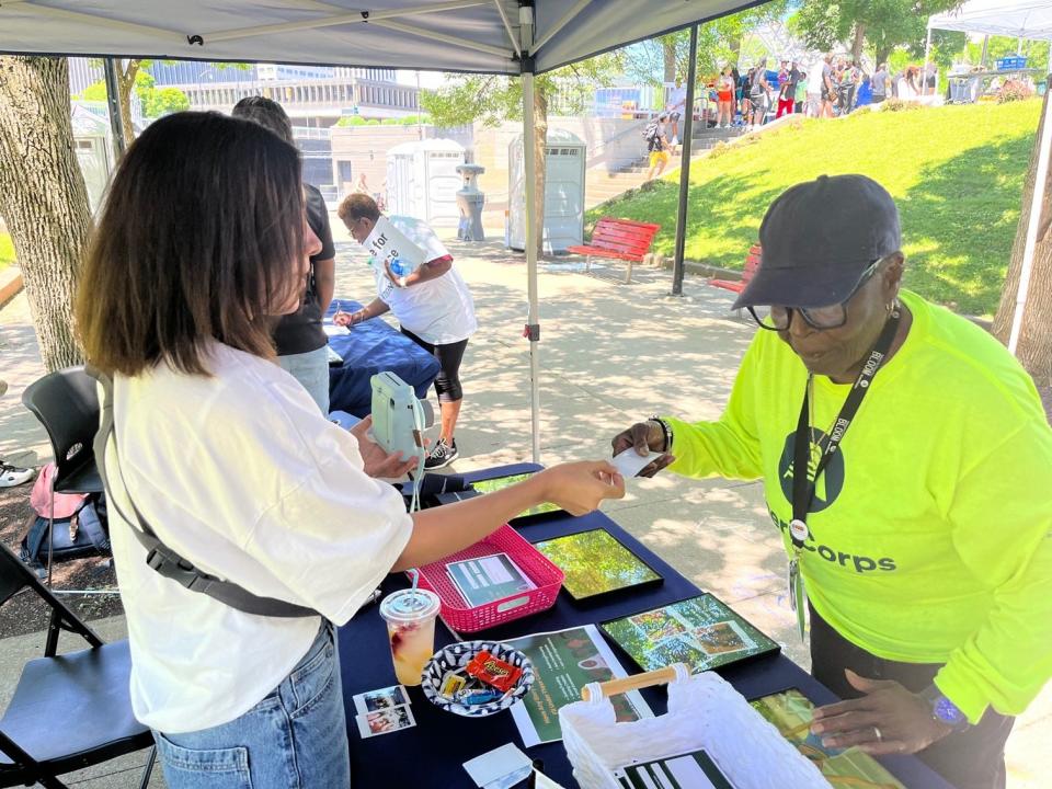 Armenian journalist Lucy Manvelian, at left, hands an instant photo to a Rochester Juneteenth festival-goer who filled out a Democrat and Chronicle story idea survey. Manvelian was here thanks to a partnership with the U.S. Embassy in Yerevan and the Poynter Institute.