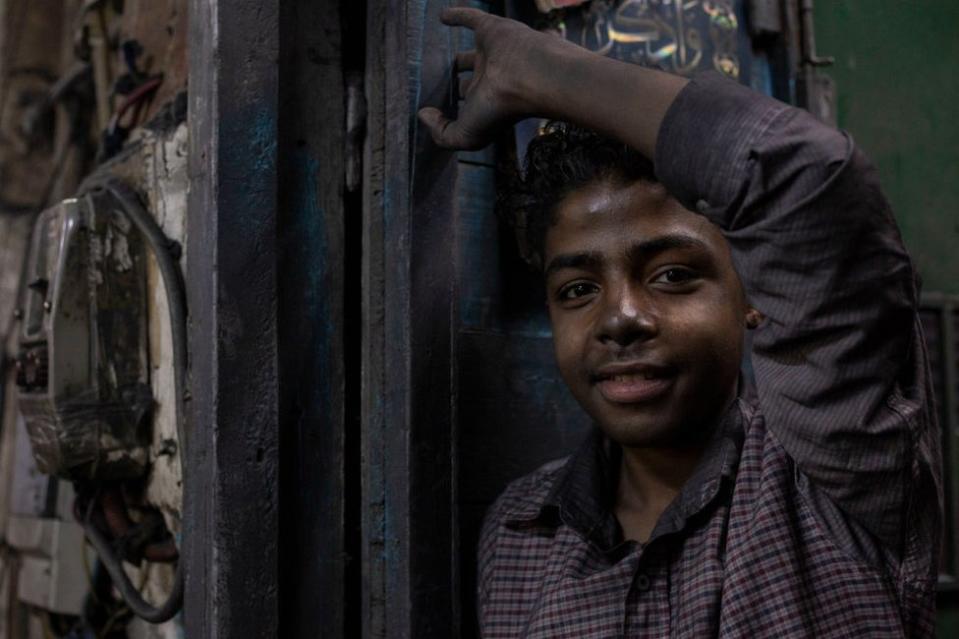 A boy with sooted hands stands at the doorway to an aluminium workshop.