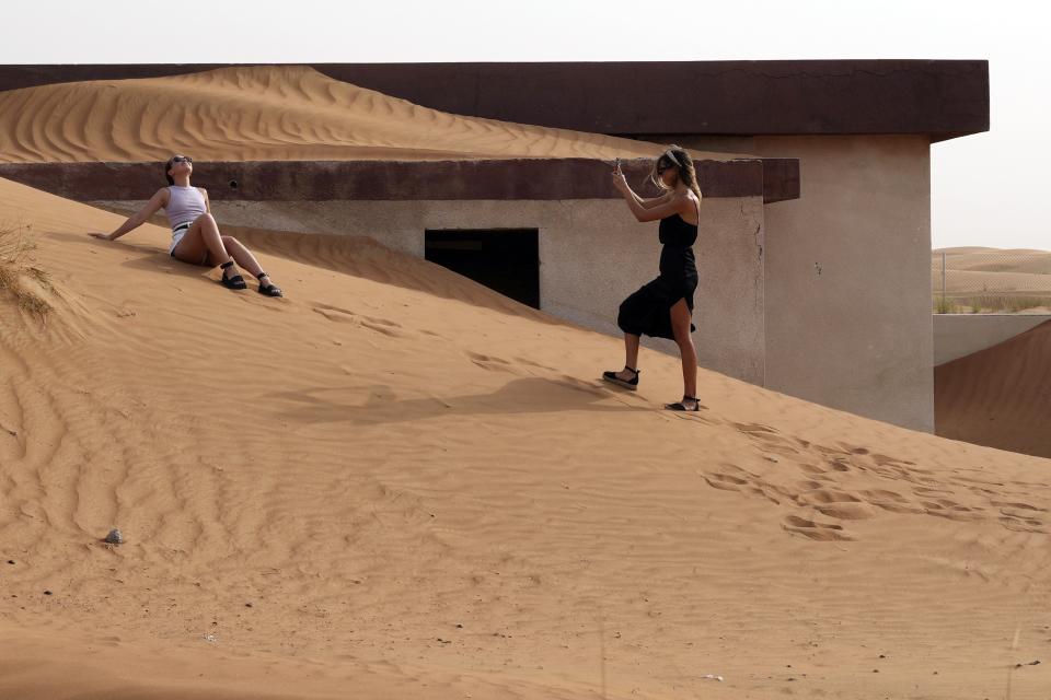 A woman poses for a photo in front of a house buried under the sand at the Bedouin village of al-Ghuraifabout 100 km, 62 miles, southeast of Sharjah, United Arab Emirates, Sunday, July 9, 2023. Built-in the 1970s, the village was abandoned two decades later as oil wealth transformed the country into a global hub of commerce and tourism, home to the futuristic cities of Dubai and Abu Dhabi. (AP Photo/Kamran Jebreili)