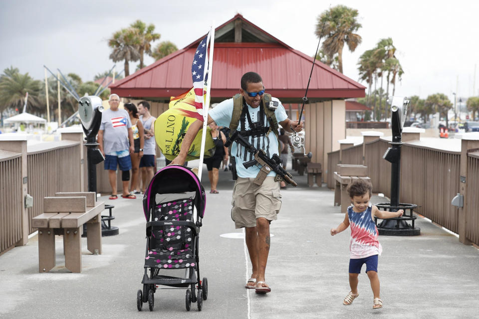 FILE - Michael Taylor, also known as "The Armed Fisherman" walks along Pier 60 with his 2-year-old daughter Ocean, his assault rifle and fishing gear on July 3, 2021, in Clearwater Beach, Fla. Under a new law beginning July 1, 2023, anyone who’s legally able to own a gun can carry it concealed without a permit. In May 2023, you need a permit in order to carry a gun, and you have to go through training and a background check to carry a concealed weapon. (Octavio Jones/Tampa Bay Times via AP, File)