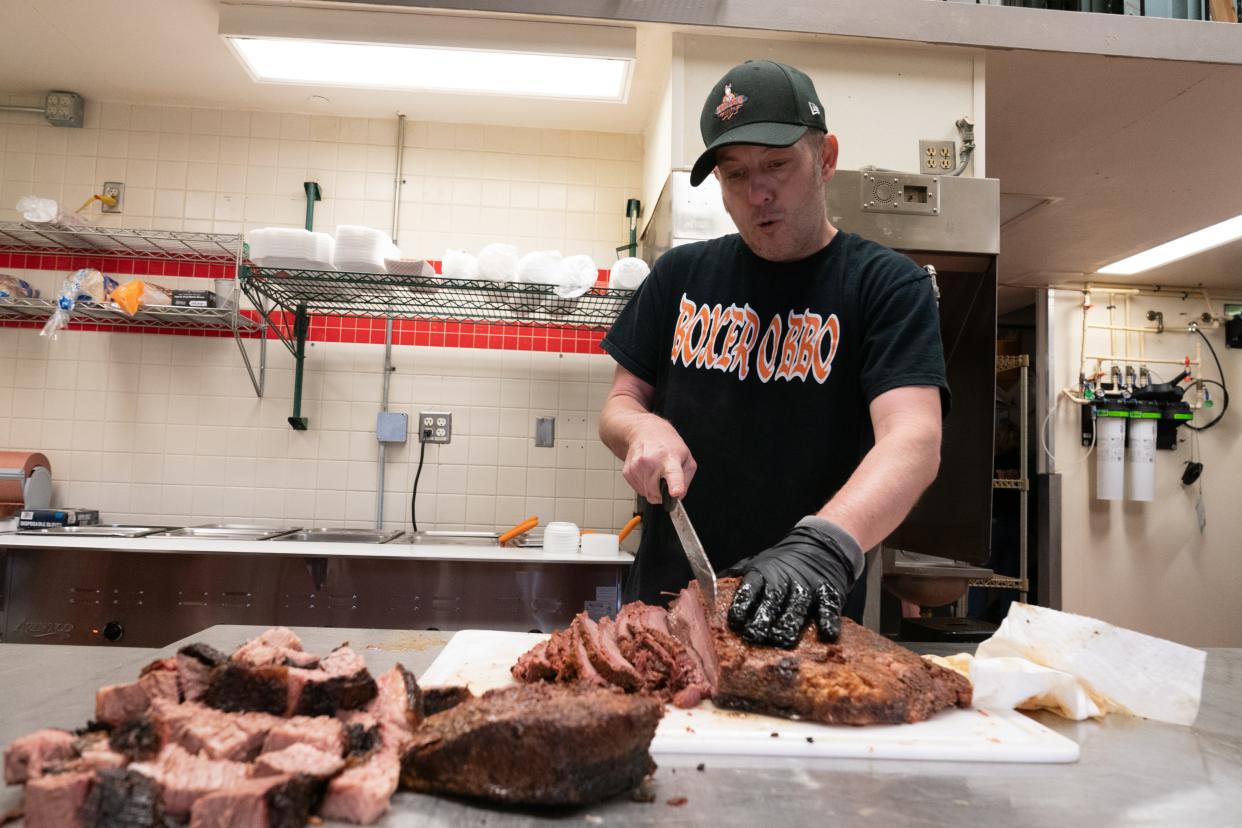 Hank Burch, co-owner of Boxer Q BBQ, cuts up pieces of brisket as he opens for business Friday morning at West Ridge Mall. Burch said he smokes the brisket for 10 hours before it's ready to serve.