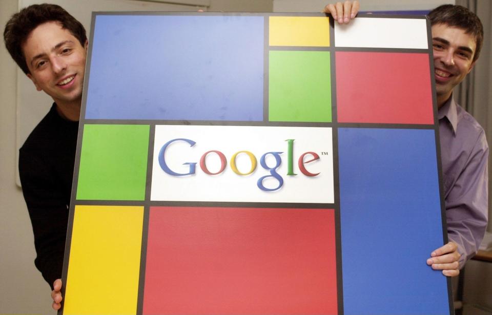 Sergey Brin and Larry Page pose with a Google logo in a Piet Mondrian abstract style, peeking out from either side of the large display, in September 2003.