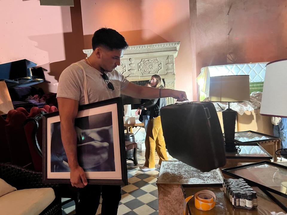 A shopper at the Gramercy Park Hotel liquidation sale holding artwork and looking at luggage.