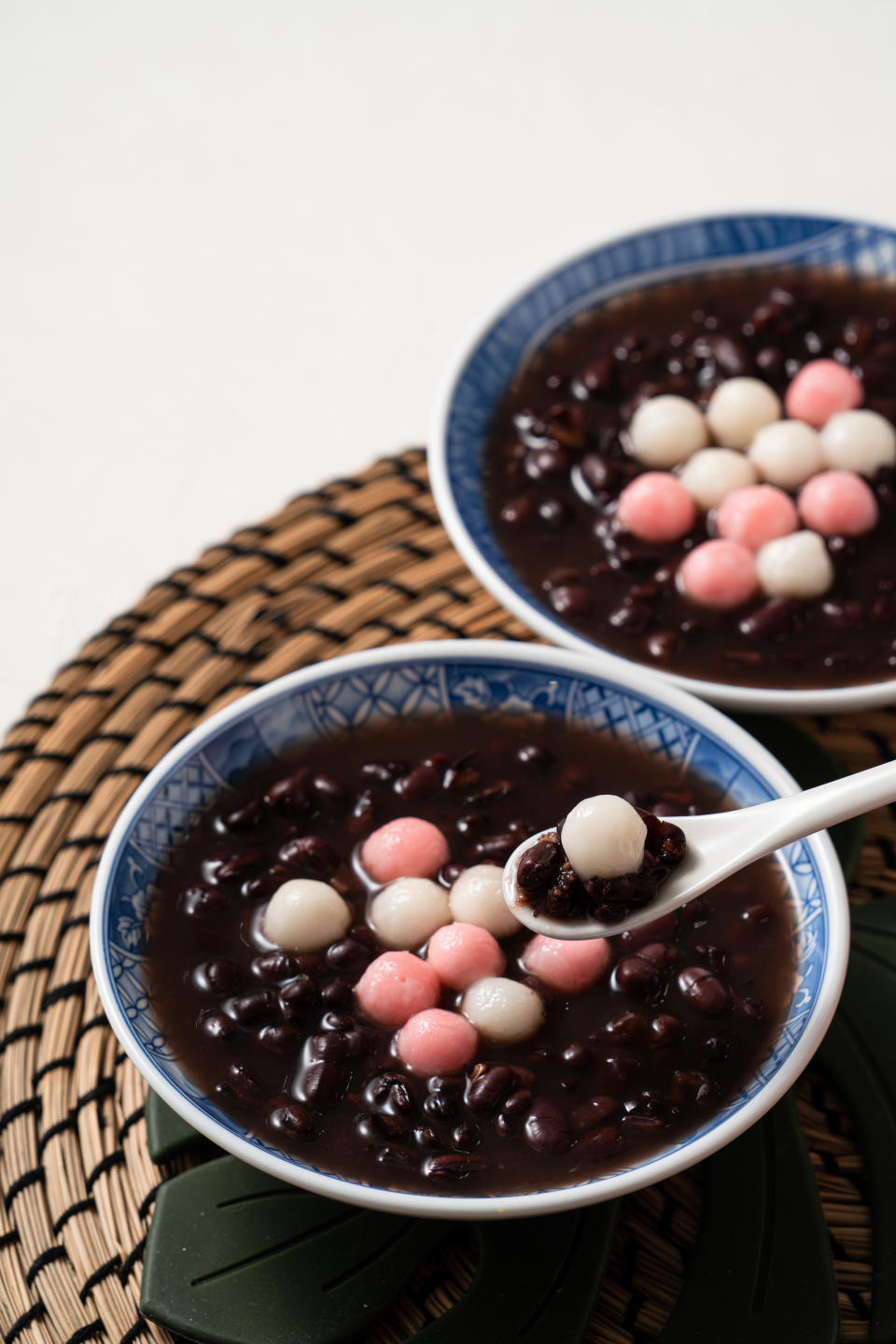 Close up of red and white tangyuan (tang yuan, glutinous rice dumpling balls) with sweet red bean soup in a bowl on white table background for Winter solstice festival food.