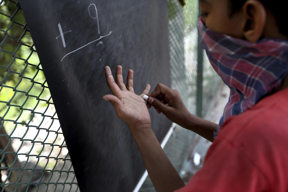 A boy learns addition on a sidewalk class taught by an Indian couple, Veena Gupta and her husband Virendra Gupta, in New Delhi, India, on Sept. 3, 2020. It all began when Veena's maid complained that with schools shut, children in her impoverished community were running amok and wasting time. The street-side classes have grown as dozens of children showed keen interest. Now the Guptas, with help from their driver, teach three different groups three times a week, morning and evening. As most schools in India remain shut since late March when the country imposed a nationwide lockdown to curb the spread of COVID-19, many switched to digital learning and taking classes online. (AP Photo/Manish Swarup)