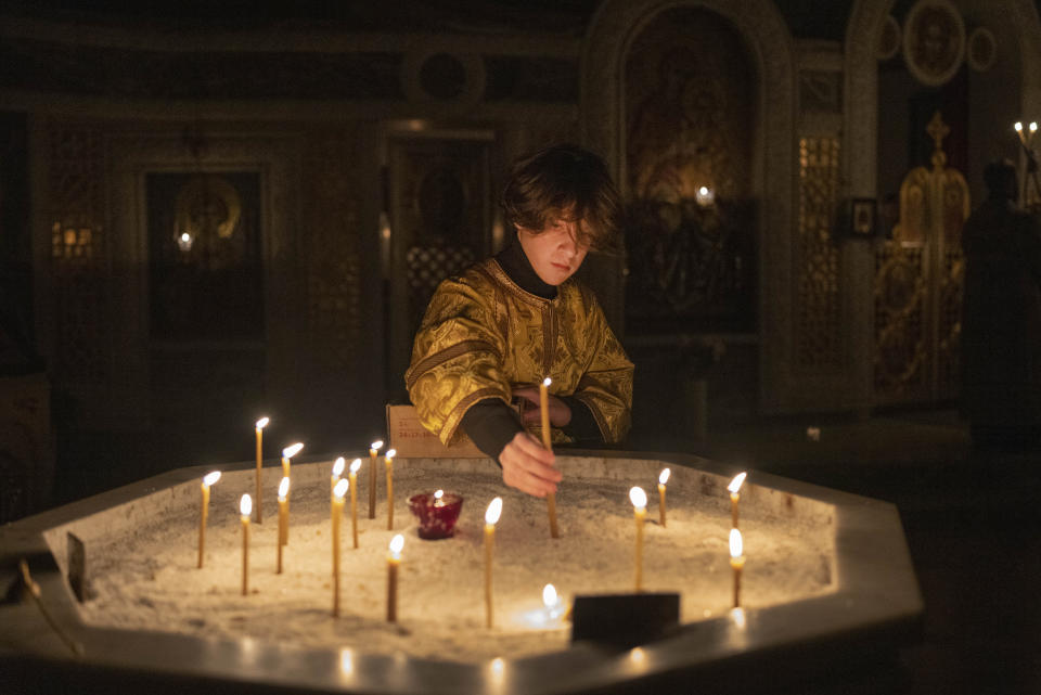 A young priest places a candle during a religious service inside the Transfiguration of Jesus Orthodox Cathedral during a blackout caused by recent Russian rocket attacks, in Kyiv, Ukraine, Saturday, Dec. 3, 2022. A top Orthodox priest in Ukraine's capital says he supports the efforts of President Volodymyr Zelenskyy's government and counter-intelligence agency to end Russian spying and meddling in Ukrainian politics through a Moscow-affiliated church. (AP Photo/Efrem Lukatsky)