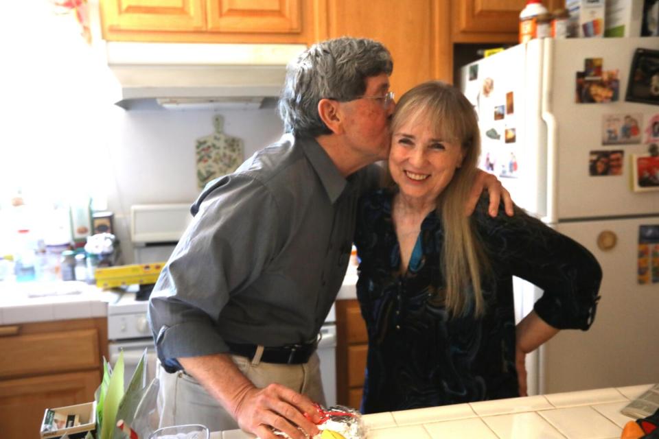 A man kisses his partner in the kitchen of their home.