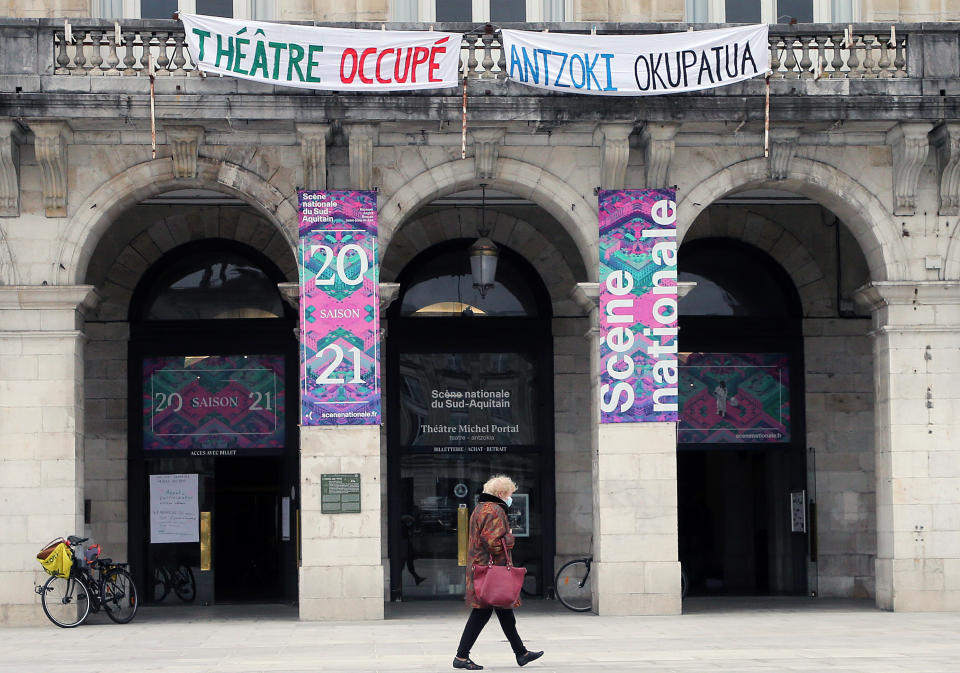 A woman walks past a theater with signs showing it occupied by culture workers, actors students and theater employees in Bayonne, southwestern France, Friday, March 26, 2021. French theaters, cinemas, museums and tourist sites have been closed for much of the past year as part of government virus protection measures, and no reopening plans have been announced. (AP Photo/Bob Edme)