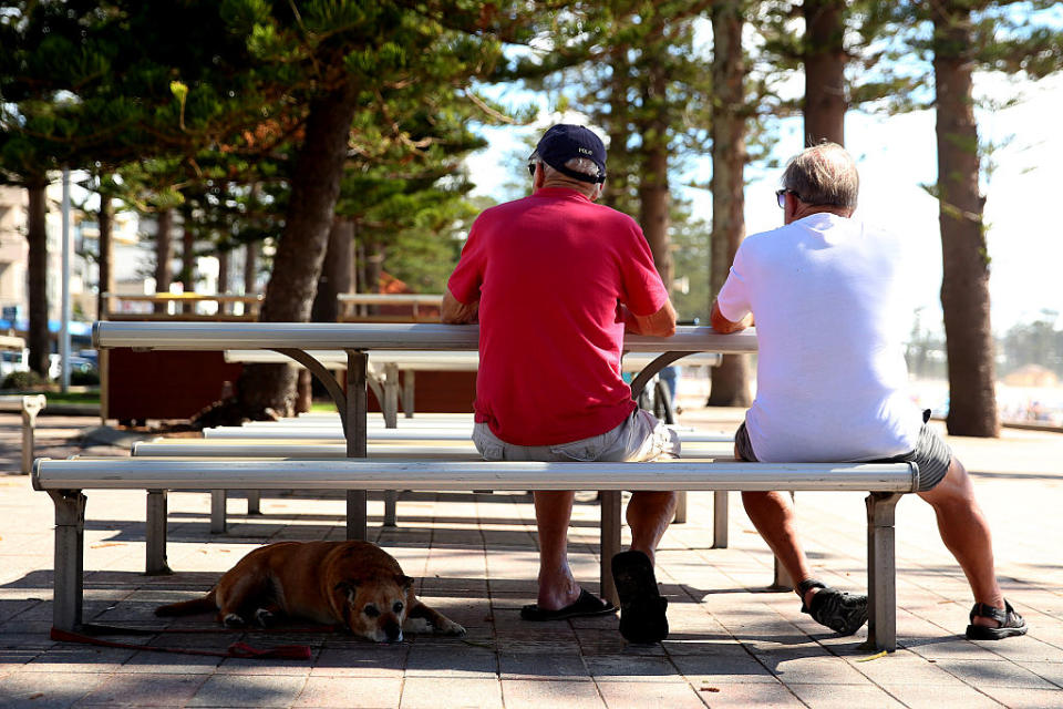 A dog rests in the shade as men sit at a picnic bench in Sydney. Source: Getty