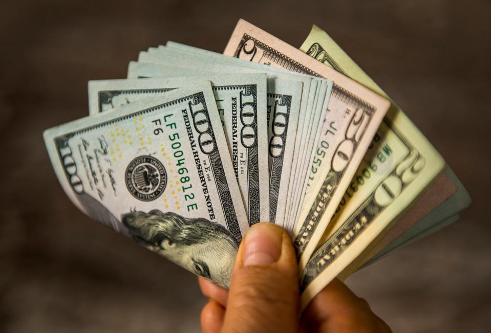 A person holding a folded, fanned-out assortment of banknotes by their fingertips.