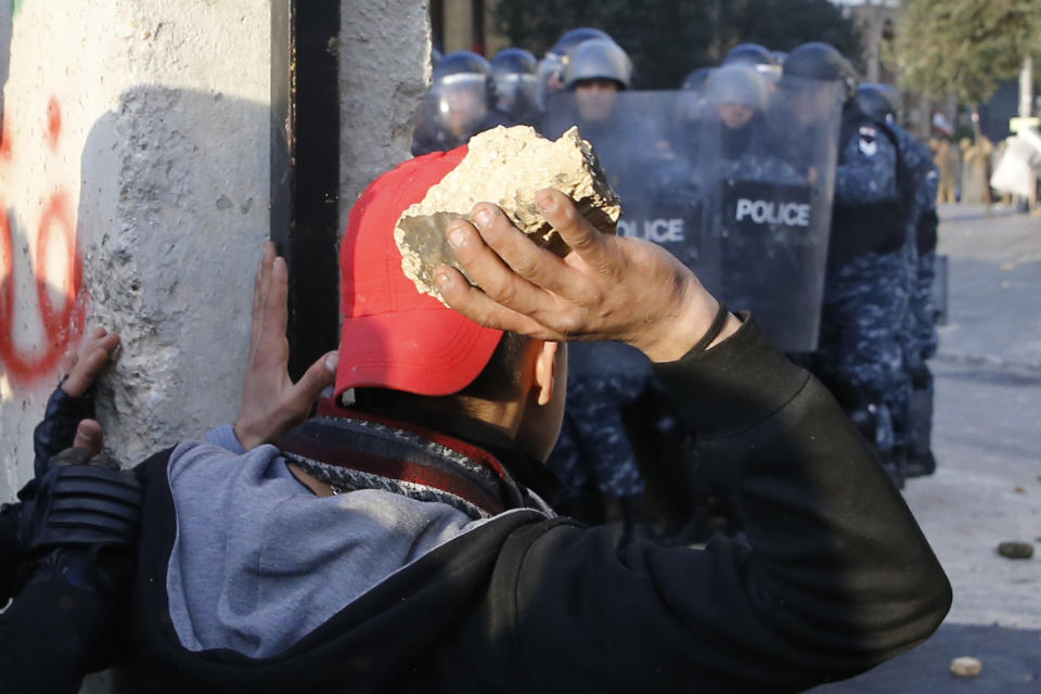 Anti-government demonstrators prepare to throw stones toward riot police at a road leading to the parliament building, during a protest against a parliament session to vote of confidence for the new government, in downtown Beirut, Lebanon, Tuesday, Feb. 11, 2020. (AP Photo/Bilal Hussein)