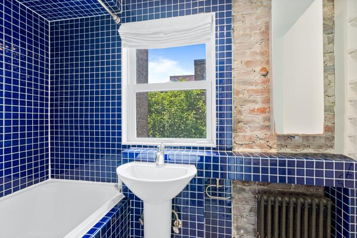 حمامی با کاشی کاری های آبی کوچک و پنجره ای بالای سینک