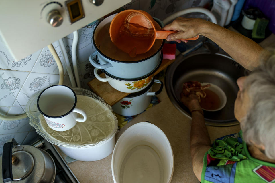 Lyubov Mahlii, 76, takes water stored in pots to use for cooking in her apartment in Sloviansk, Donetsk region, eastern Ukraine, Sunday, Aug. 7, 2022. Mahlii said she boils some water for at least 15 minutes to make sure it's safe for consumption. (AP Photo/David Goldman)