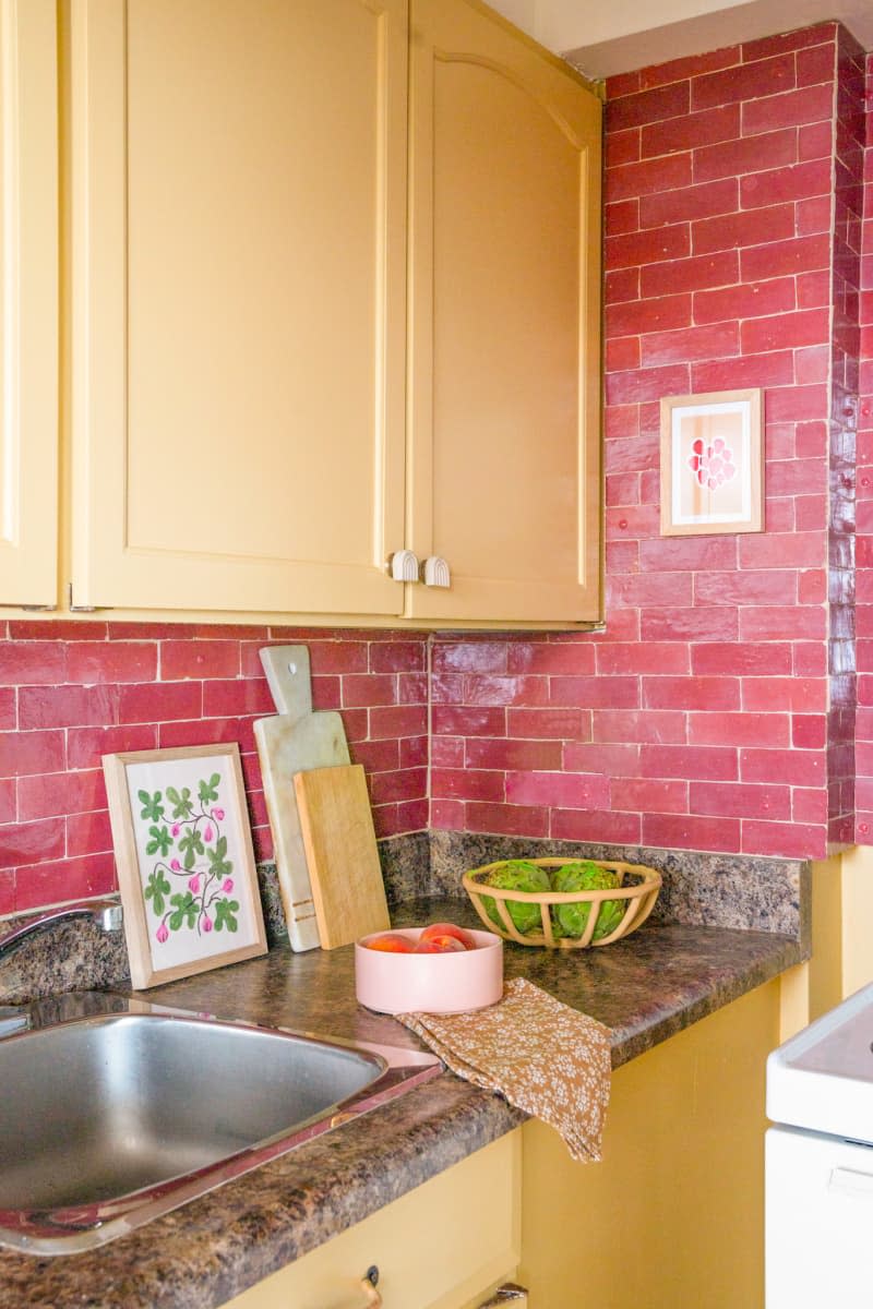Kitchen with yellow painted cabinets, a red tile backsplash, and dark brown speckled countertops