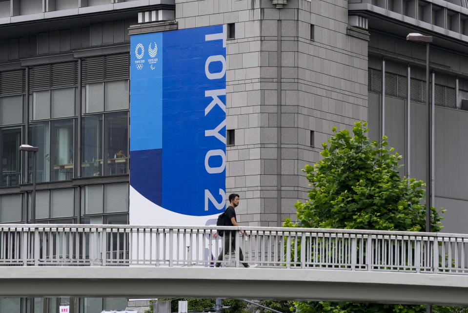 A person wearing a protective mask walks over a pedestrian bridge as Tokyo 2020 banner is seen on a side of a building Wednesday, June 23, 2021, in Tokyo. (AP Photo/Kiichiro Sato)