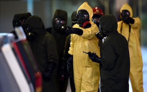 Malaysian police in chemical warfare suits investigate the crime scene - Credit: MANAN VATSYAYANA/AFP