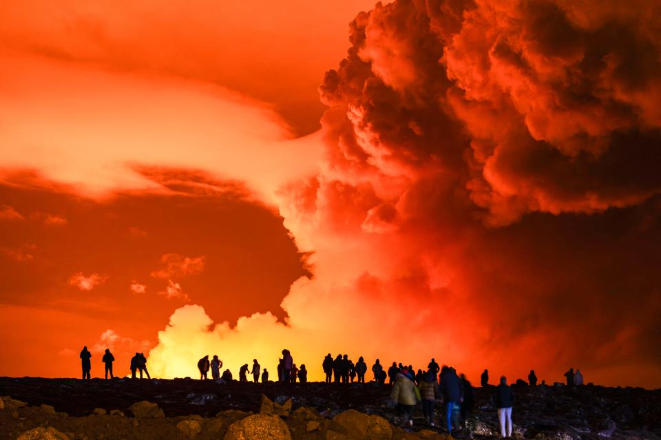 People gather to watch as molten lava flows out from a fissure on the Reykjanes peninsula north of the evacuated town of Grindavik, western Iceland on March 16, 2024. Lava spewed Saturday from a new volcanic fissure on Iceland's Reykjanes peninsula, the fourth eruption to hit the area since December, authorities said.