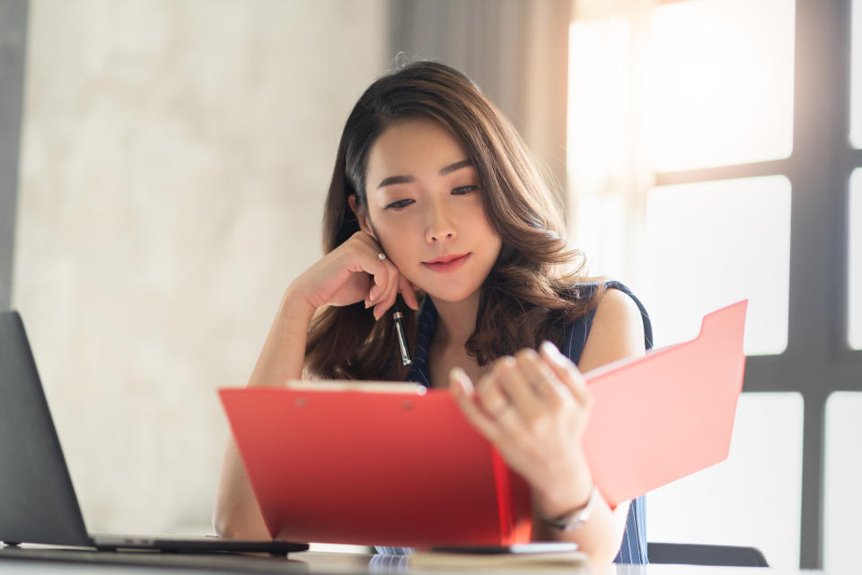 Portrait of smiling pretty young business woman holding and looking at a red clipboard, document folder. Asian female working in the office.