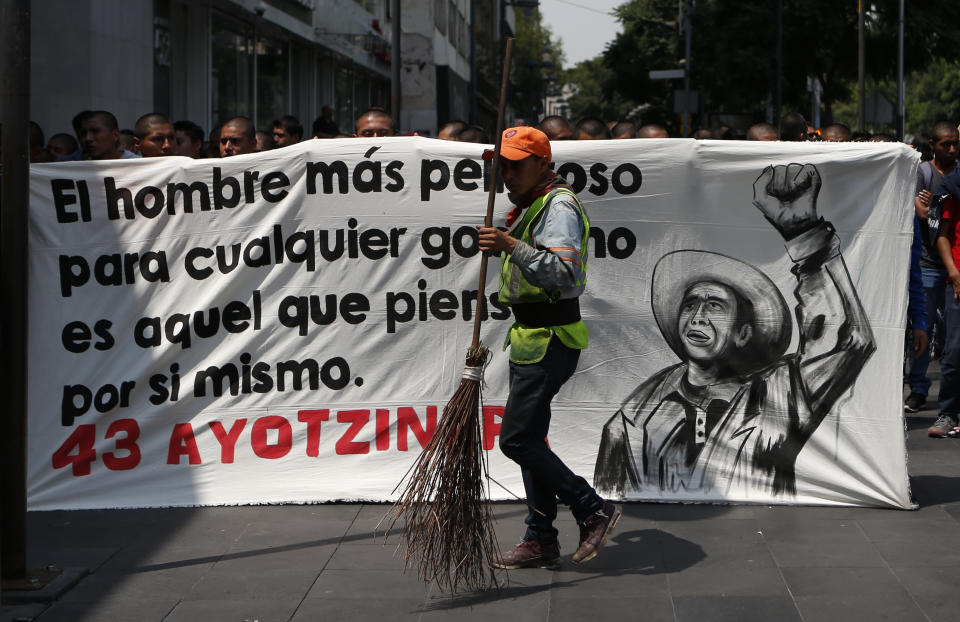 A city cleaner walks past a banner reading, in Spanish, "The most dangerous man for any government is he who thinks for himself," as students demonstrate outside where President-elect Andres Manuel Lopez Obrador was meeting with parents of college students on the fourth anniversary of the students' disappearance at the hands of police, at the Memory and Tolerance Museum in Mexico City, Wednesday, Sept. 26, 2018. Lopez Obrador said Wednesday his administration will accept a truth commission to investigate the case of 43 teachers-college students missing since Sept. 26, 2014, drawing rare praise and expressions of hope from the long-suffering parents of the victims.(AP Photo/Rebecca Blackwell)