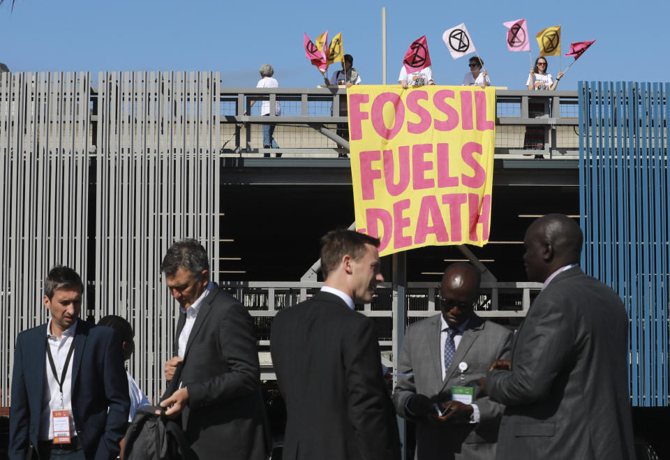 FILE - Climate activists from Extinction Rebellion hold a placard as they protest at the Africa Energy Week conference, foreground, in Cape Town, South Africa, Oct. 20, 2022. A new report from doctors and other health experts says the world's fossil fuel addiction is making the world sicker and is killing people. (AP Photo/Nardus Engelbrecht, File)
