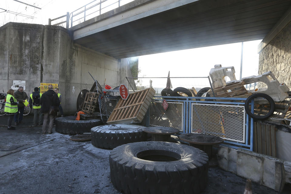 Demonstrators stand near a makeshift barricade set up by the so-called yellow jackets to block the entrance of a fuel depot in Le Mans, western France, Tuesday, Dec. 5, 2018. The French government's decision to suspend fuel tax and utility hikes Tuesday did little to appease protesters, who called the move a "first step" and vowed to fight on after large-scale rioting in Paris last weekend. (AP Photo/David Vincent)