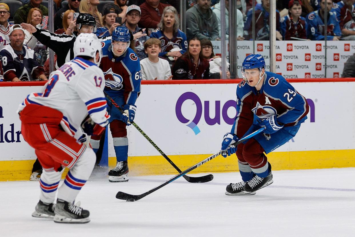Mar 28, 2024; Denver, Colorado, USA; Colorado Avalanche center Nathan MacKinnon (29) controls the puck against New York Rangers left wing Alexis Lafreniere (13) as left wing Artturi Lehkonen (62) defends in overtime at Ball Arena.