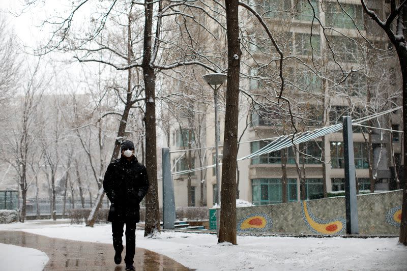 A man wearing a face mask walks at a residential complex during a snowfall, as the country is hit by an outbreak of the new coronavirus, in Beijing