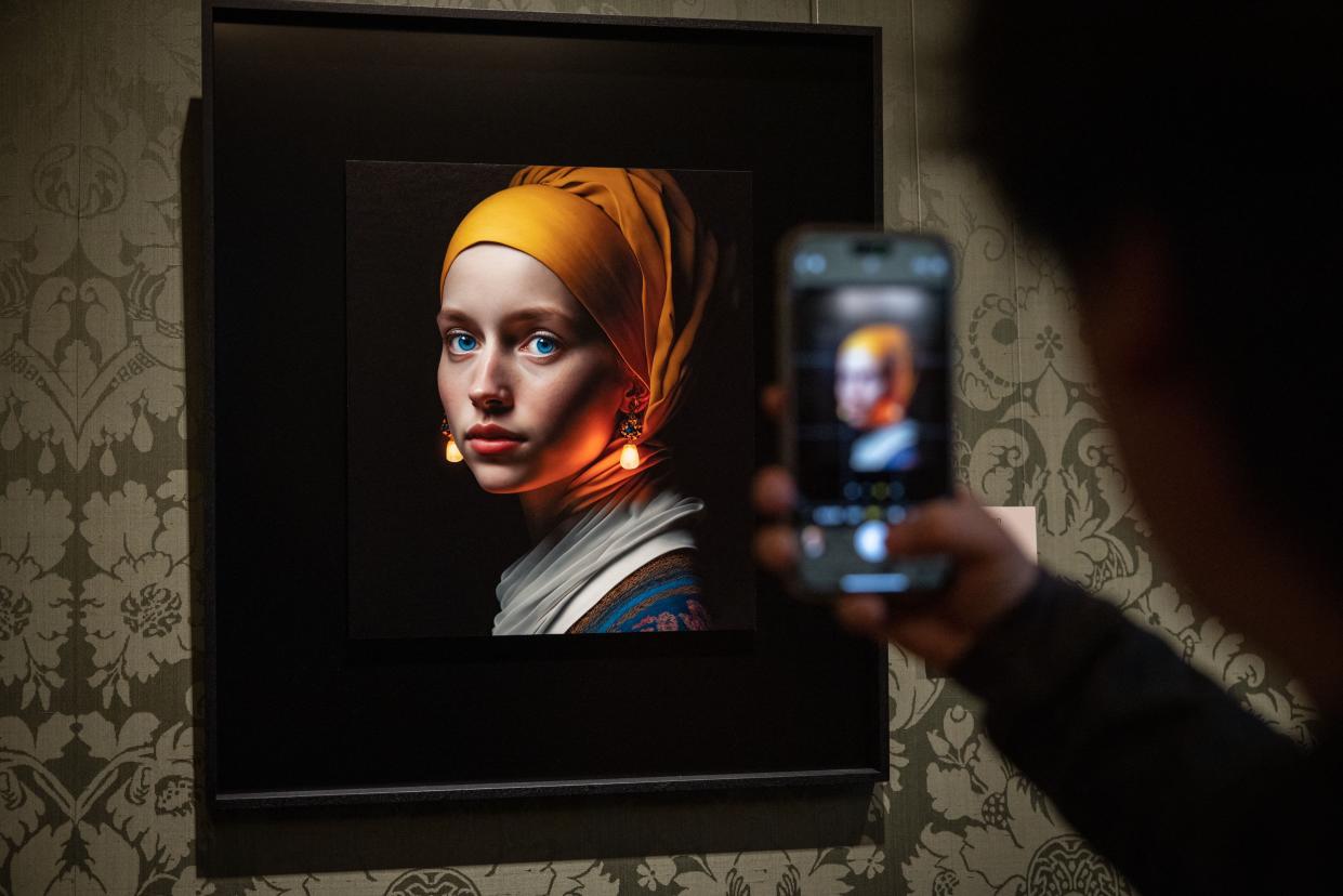A visitor takes a picture with his mobile phone of an image designed with artificial intelligence by Berlin-based digital creator Julian van Dieken (C) inspired by Johannes Vermeer's painting "Girl with a Pearl Earring" at the Mauritshuis museum in The Hague on March 9, 2023. - Julian van Dieken's work made using artificial intelligence (AI) is part of the special installation of fans' recreations of Johannes Vermeer's painting "Girl with a Pearl Earring" on display at the Mauritshuis museum.