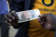 Street vendors hold the new currency note called the ZiG, in Harare, Zimbabwe, Tuesday, April 30, 2024. Authorities in Zimbabwe are resorting to force to defend the new currency, including packing jail cells with dozens of street currency dealers and freezing accounts of hordes of businesses accused of undermining the value of the ZiG. (AP Photo/Tsvangirayi Mukwazhi)