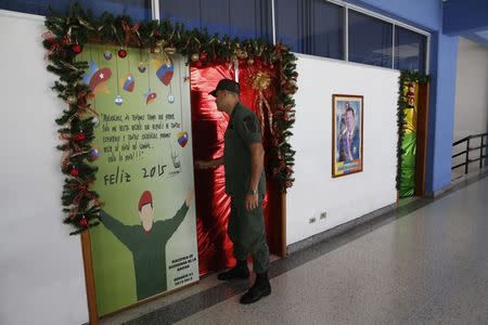 A Venezuelan soldier opens a door decorated for Christmas with an image depicting Venezuela's late President Hugo Chavez as he arrives to attend a lecture of the academic course, "Studies of the Thoughts of the Supreme Commander Hugo Chavez" in Caracas November 19, 2014. REUTERS/Carlos Garcia Rawlins