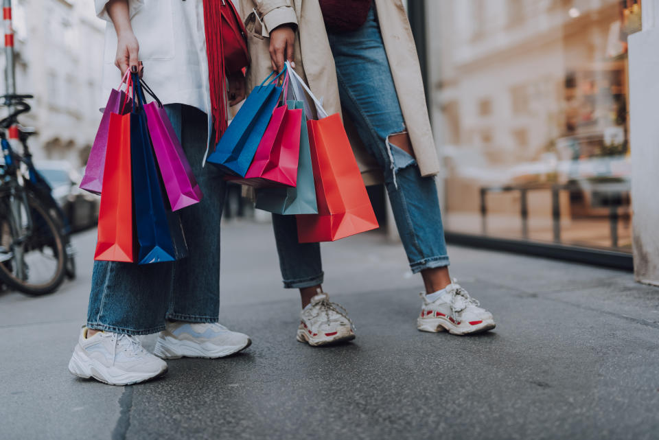 Look what we bought. Close up of two girl in jeans and sneakers holding colorful shopping bags