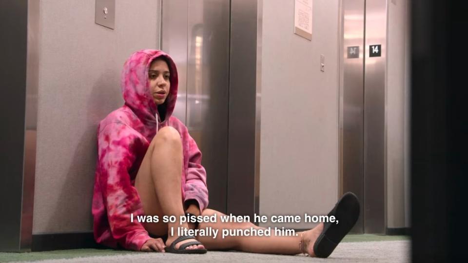 Rae sits by an elevator and says, "I was so pissed when he came home, I literally punched him"