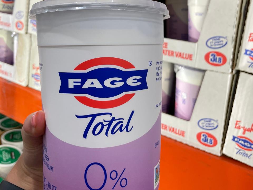 hand holding white and purple tub of fage greek yogurt at costco