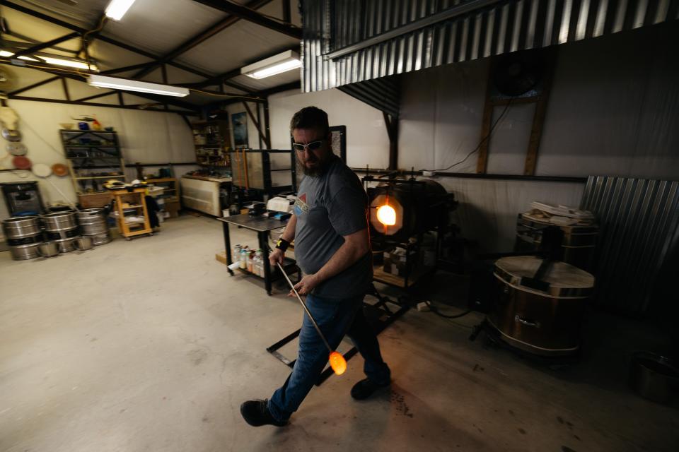 Eric Minton walks back to his bench after gathering molten glass on the end of his pipe.