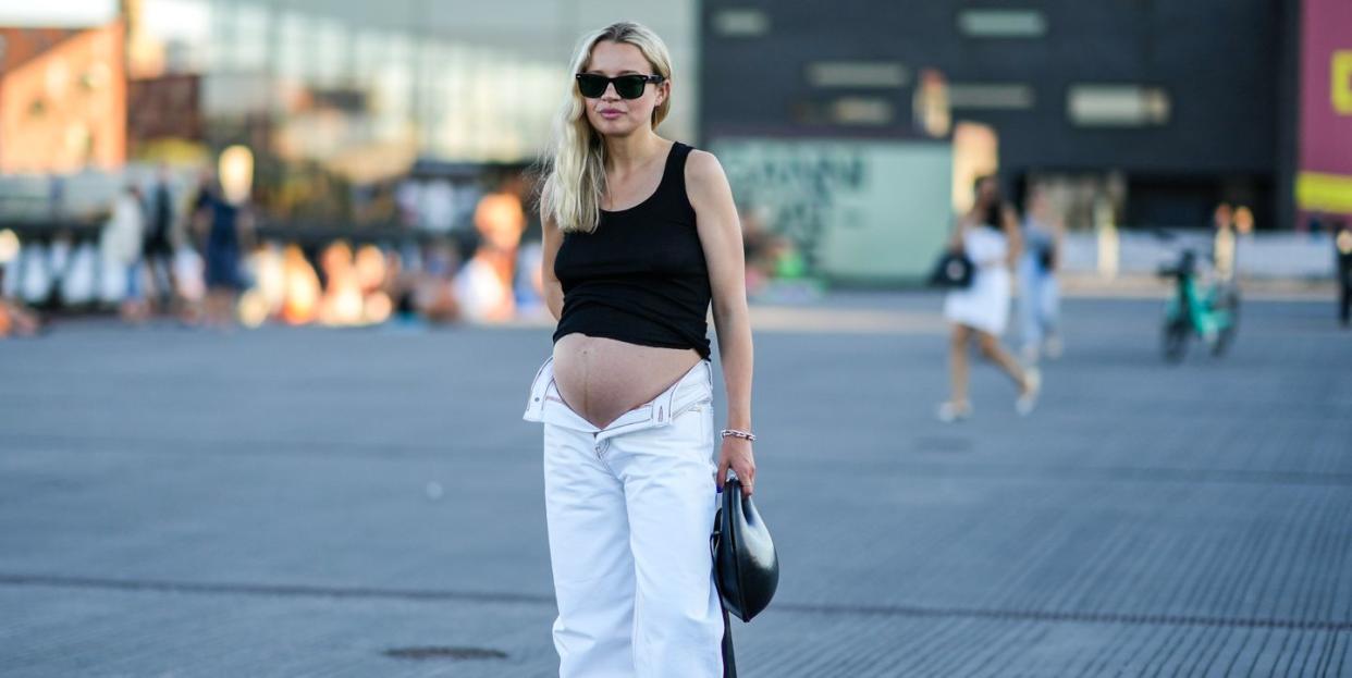 copenhagen, denmark august 11 a guest wears black sunglasses, a black tank top, a silver large chain bracelet, rings, a black shiny leather ball handbag, open white denim large pants, black shiny leather mules  shoes , outside ganni, during copenhagen fashion week springsummer 2023, on august 11, 2022 in copenhagen, denmark photo by edward berthelotgetty images