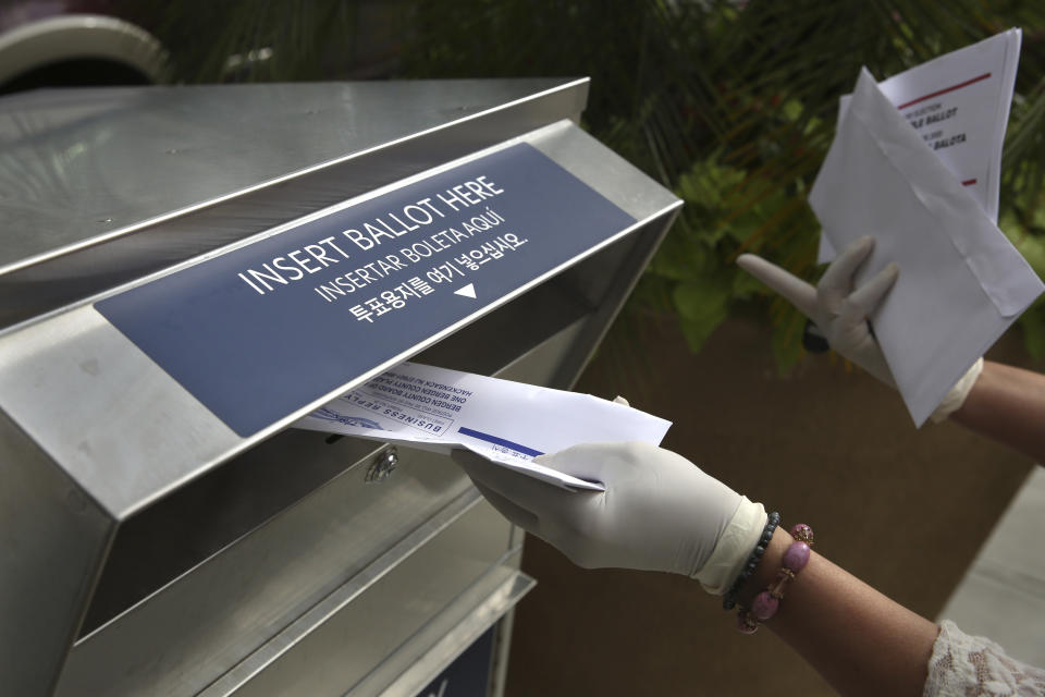 FILE - In this July 7, 2020, file photo a woman wearing gloves drops off a mail-in ballot at a drop box in Hackensack, N.J. The November election is coming with a big price tag as America faces the coronavirus pandemic. The demand for mail-in ballots is surging, election workers are in need of training and polling booths might have to be outfitted with protective shields. (AP Photo/Seth Wenig, File)