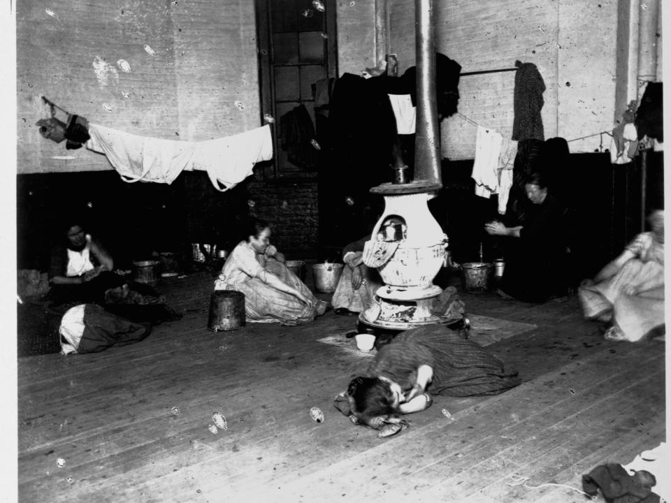 A group of women and children hang clothes and rest on the floor of a Manhattan police station their temporary home, circa 1890.