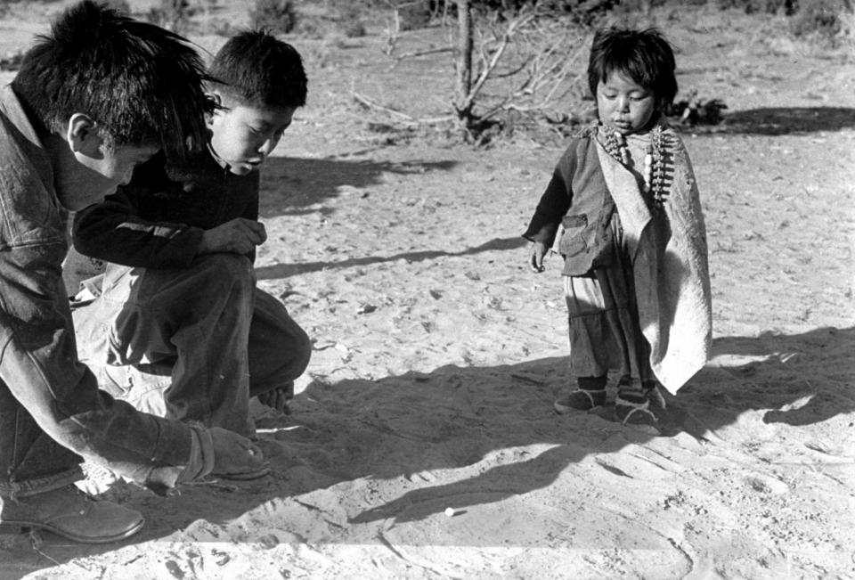 <b>Caption from LIFE.</b> Game of marbles, one popular part of white man's culture, is explained by small boy at center to brother and sister. This boy goes to school and learned the game there. His brother has to stay home to help with the sheepherding.