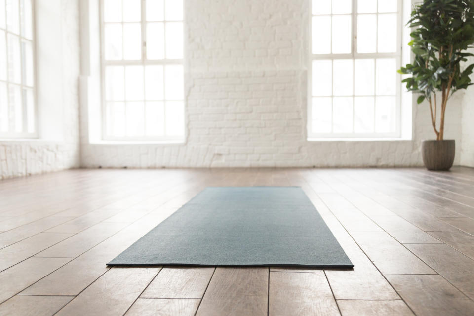 Empty room in yoga studio with unrolled yoga mat on wooden floor, modern fitness center with big windows and white brick walls, sport equipment for meditating or sport exercises close up