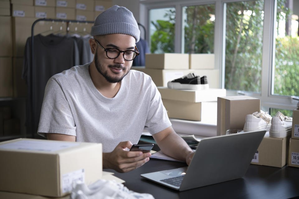 Asian man online seller confirming orders from customer on the phone. E-commerce male business owner looking at the phone in store warehouse.