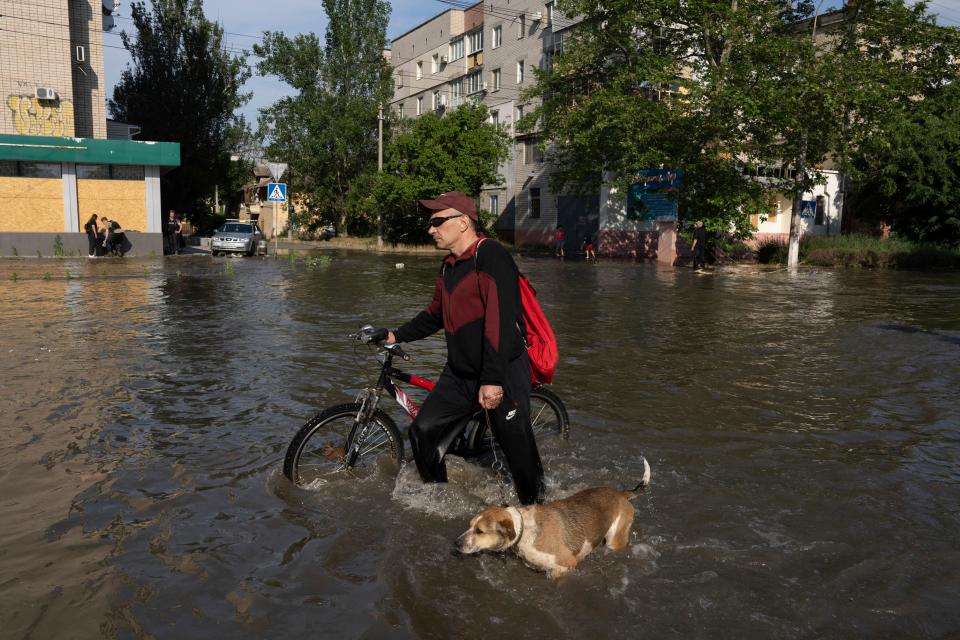 A local resident with a bike and a dog walks along the street past the buildings in Kherson, Ukraine, Tuesday, Jun 6, 2023 which were flooded after the Kakhovka dam was blown up overnight. The wall of a major dam in a part of southern Ukraine has collapsed, triggering floods, endangering Europe's largest nuclear power plant and threatening drinking water supplies. (AP Photo/Evgeniy Maloletka) ORG XMIT: XEL128