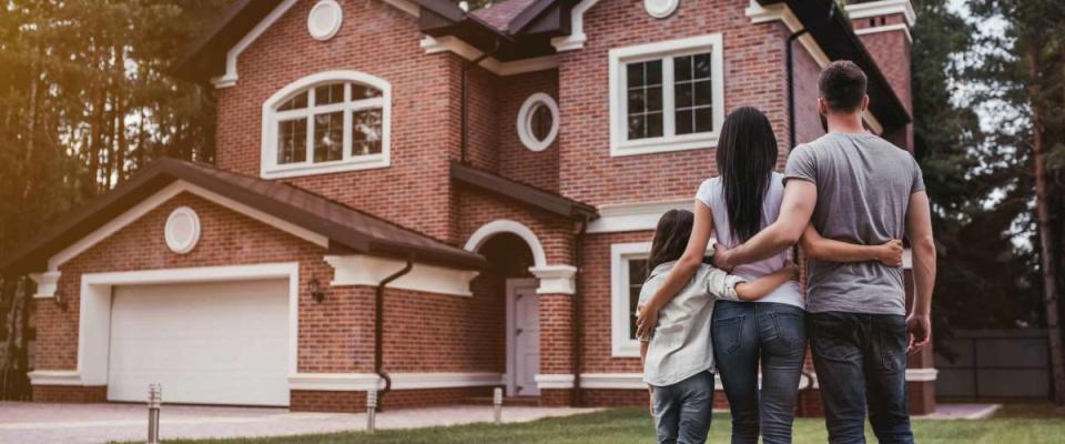 Back view of happy family is standing near their modern house and hugging