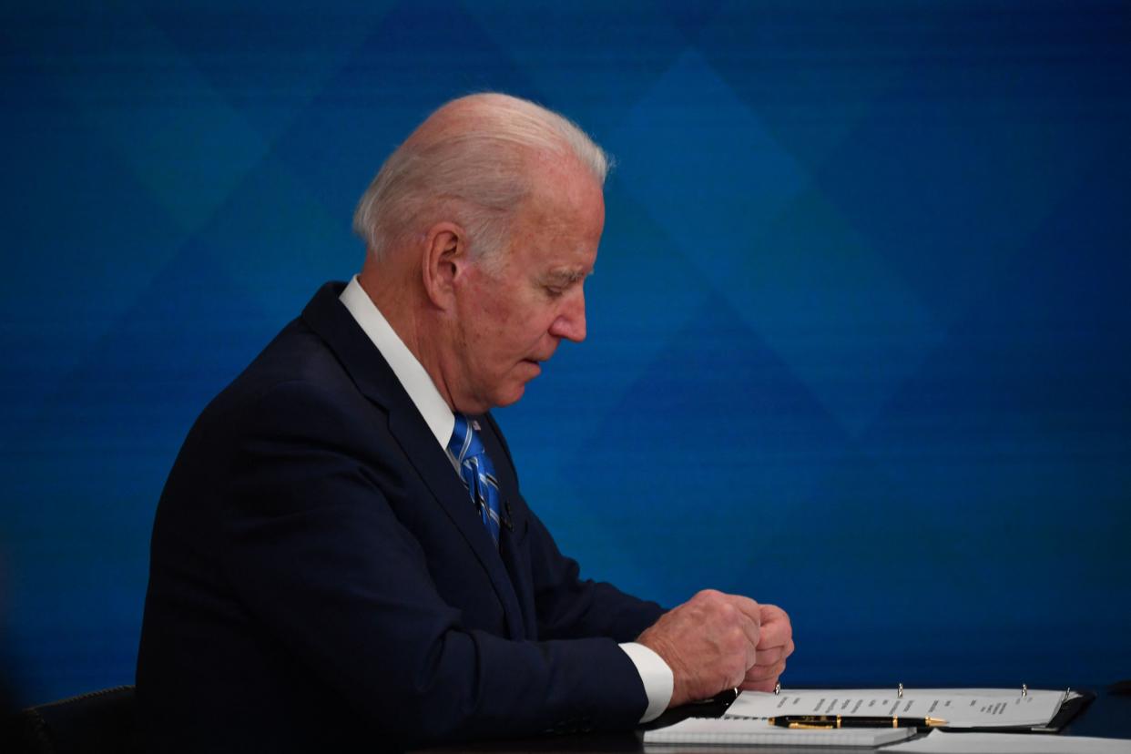 President Biden looks down at notes on the desk in front of him during a conference call.