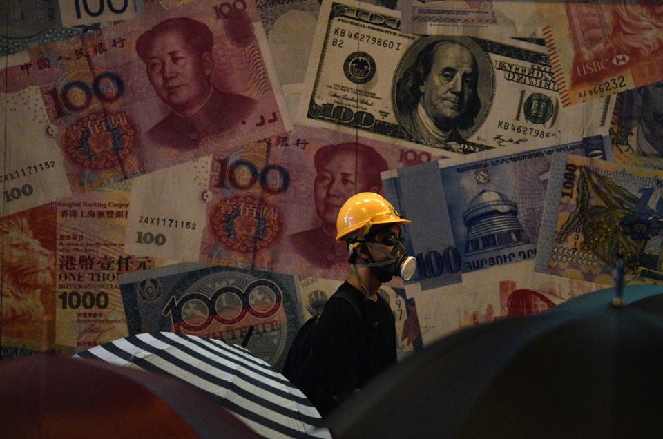A protester stands next to images of currency notes on the side of a building during a demonstration against a controversial extradition bill in Hong Kong on July 28, 2019. - Tens of thousands of pro-democracy protesters defied authorities to hold an unsanctioned march through Hong Kong, a day after riot police fired rubber bullets and tear gas to disperse another illegal gathering, plunging the financial hub deeper into crisis. (Photo by Anthony WALLACE / AFP)        (Photo credit should read ANTHONY WALLACE/AFP/Getty Images)