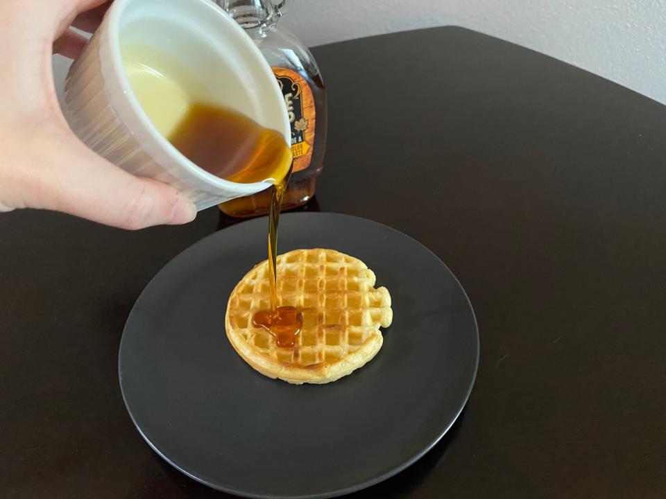 hand pouring ramekin of kroger private selection maple syrup over a toaster waffle