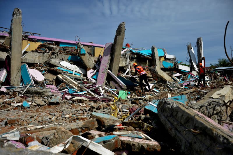 Rescue workers search for victims among the ruins of a hospital building collapsed following an earthquake in Mamuju