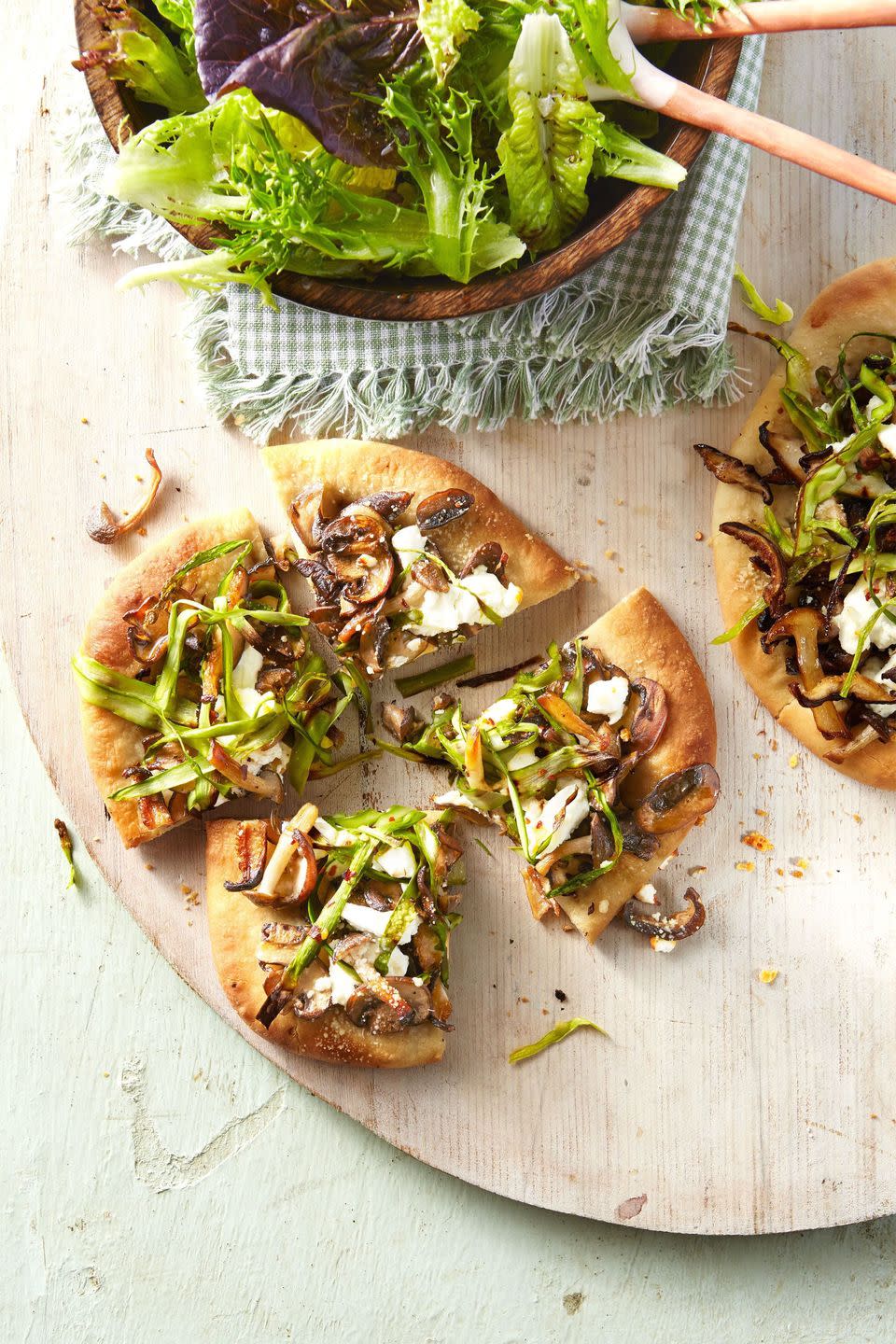 individual small mushroom and asparagus pizzas cut into four pieces on a wooden serving board